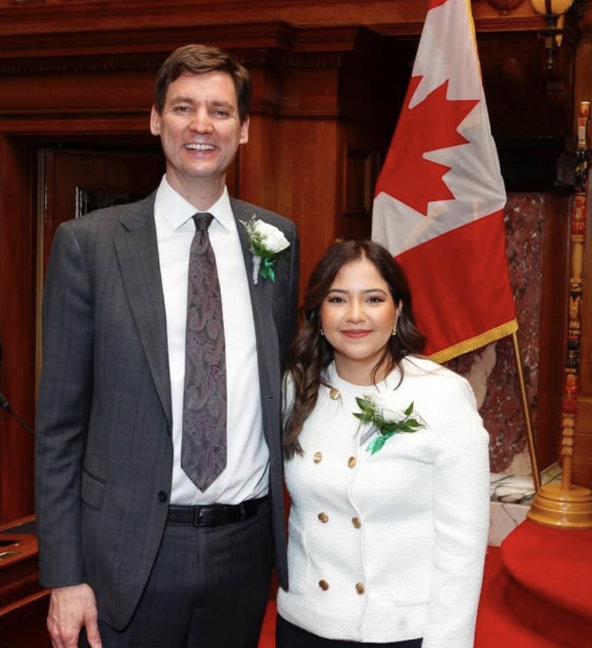 Amna Shah standing beside a colleague in front of a Canadian flag.