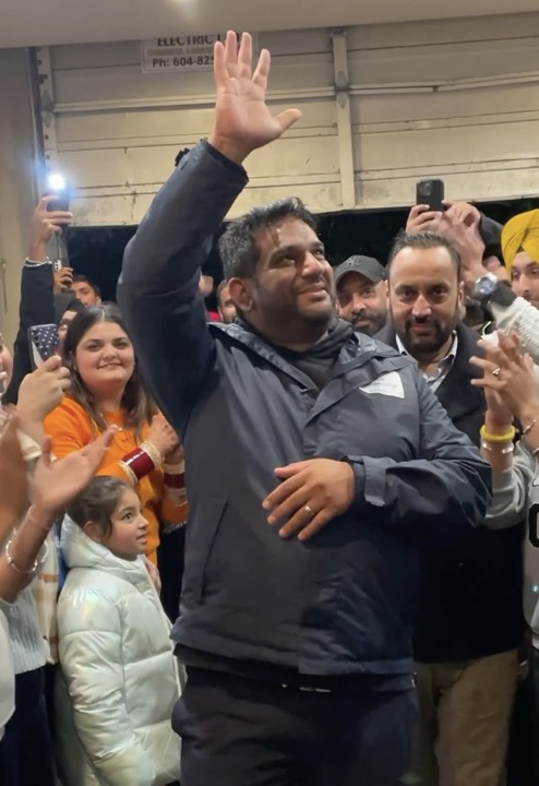Mandeep Dhaliwal waving to people at an indoor gathering.